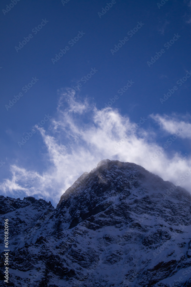 Stunning snowy peak of High Tatras in Poland, bathed in sunlight with whispy clouds hovering above against a clear blue sky. A testament to nature's majesty.