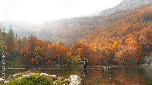 Pescando a mosca in un lago sulle alpi italiane circondato da alberi immersi nel colori dell'autunno photo
