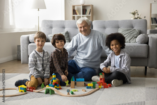 Portrait of multigenerational family sit on floor look at camera. great-grandfather spend priceless time with three multiethnic great-grandchildren, having good friendly relationships, enjoy playtime