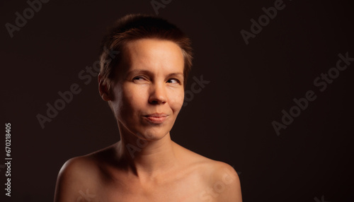 A middle-aged woman with a chic short haircut, baring her shoulders against a black backdrop. Her lovely face carries a playful expression
