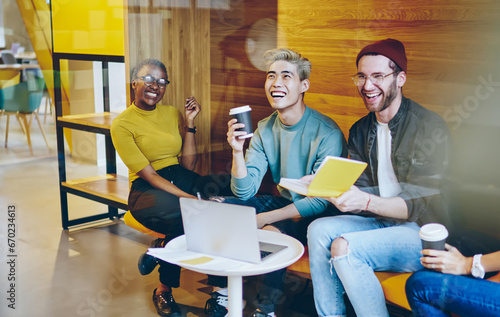 Cheerful multicultural young people laughing during coffee break in modern office