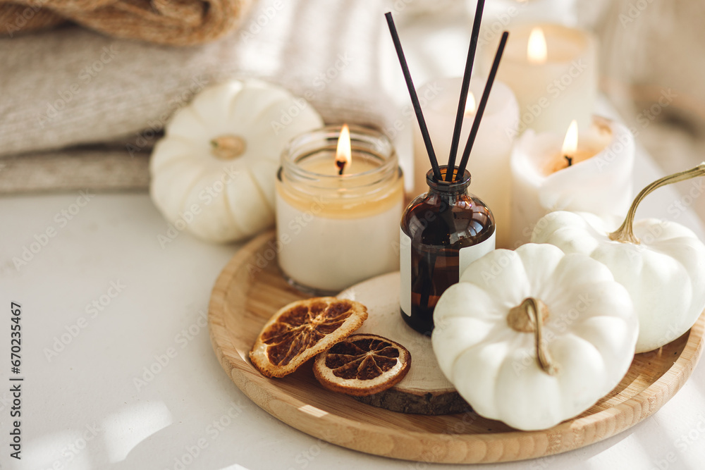 Autumn cozy mood composition on the windowsill. Aroma diffuser, pumpkins, dry citrus, candles on wooden tray, knitted warm plaid. Fall hygge home decor, aromatherapy. Copy space, white background