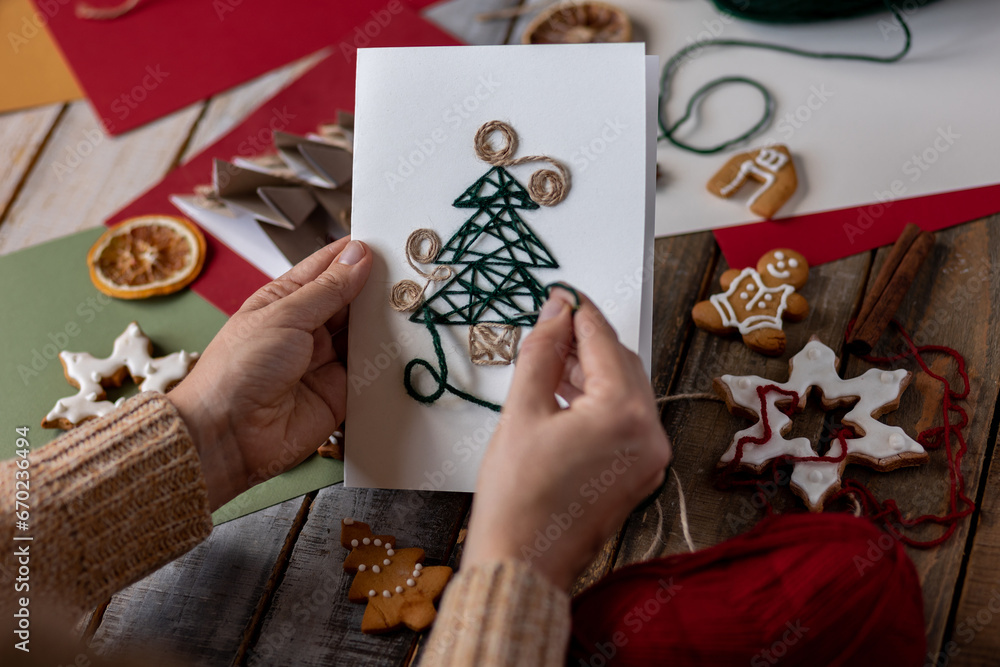 Woman creating handmade craft paper christmas card with wool thread fir tree. Idea for quality family time with children, do it yourself present, hobby, holiday leisure activity. Recyclable materials