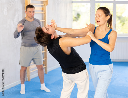 Young guy and woman train to perform effective blows and impact on pain points eyes groin while learning self-defense techniques. Lesson in presence of experienced instructor © JackF