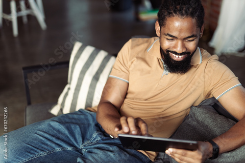 African American man relaxing on sofa at home and using digital table