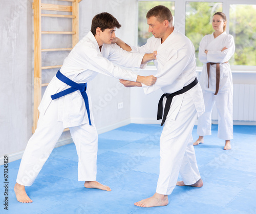 Judo or jiu-jitsu classes - two men practicing grabbing and throwing on sports mats under the guidance of a trainer