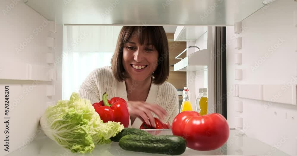 Caucasian woman opens the refrigerator and retrieves vegetables from it. Her practical approach to meal preparation is evident as she selects fresh ingredients from the fridge. Caucasian woman opens the refrigerator and retrieves vegetables from it. Her practical approach to meal preparation is evident as she selects fresh ingredients from the fridge.