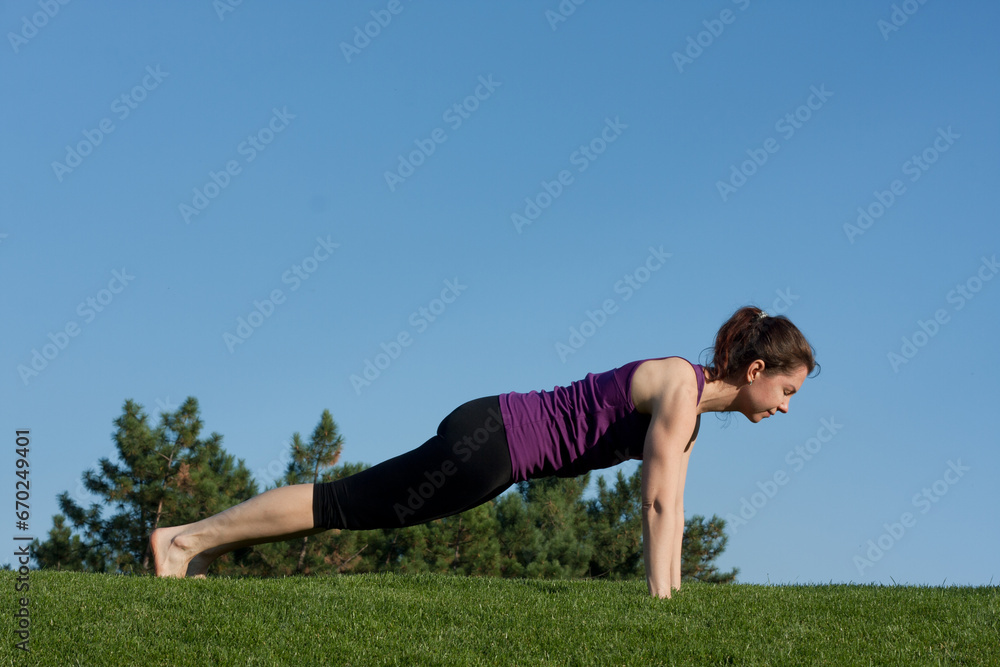 Fit young athletic woman doing static plank exercise, in city park. blue sky background on summer day. Healthy lifestyle