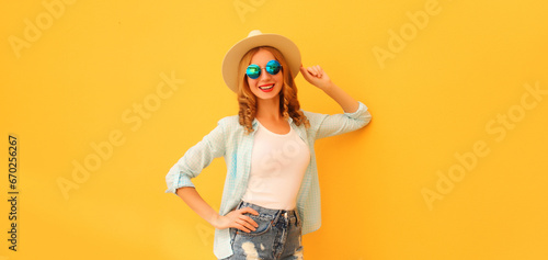 Beautiful young woman posing wearing summer straw hat and shorts on orange background