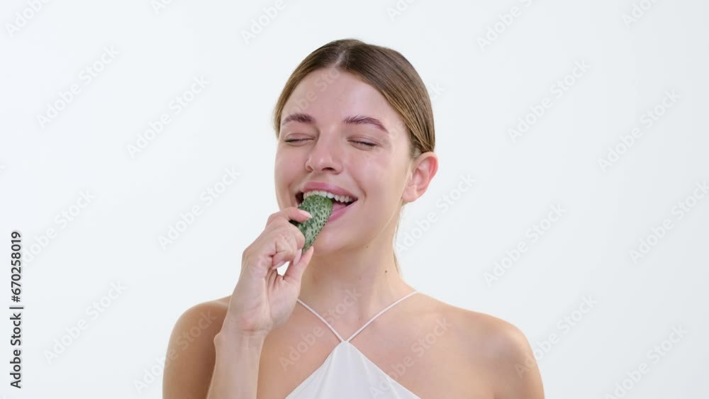 Joyful Caucasian woman takes a delightful bite into a cucumber, happiness evident in the crisp crunch of the moment. Against the white backdrop, radiant smile capture the essence of natural joy. Joyful Caucasian woman takes a delightful bite into a cucumber, happiness evident in the crisp crunch of the moment. Against the white backdrop, radiant smile capture the essence of natural joy.