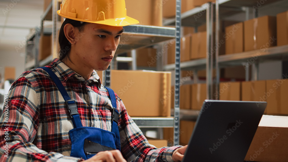 Asian man checking merchandise quality in warehouse, working on shipment and delivery with laptop. Young worker analyzing inventory for distribution management, small business concept. Asian man checking merchandise quality in warehouse, working on shipment and delivery with laptop. Young worker analyzing inventory for distribution management, small business concept.