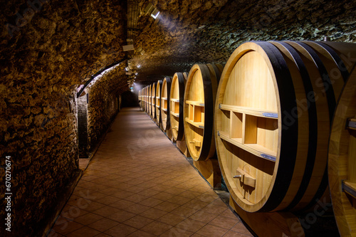 Underground wine cellars with barrels for aging of red dry wine in Chateauneuf-du-Pape wine making village in France with green vineyards on large pebbles galets and sandstone clay soil