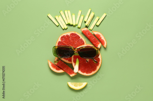 Funny face made of fruits, vegetables and sunglasses on green background