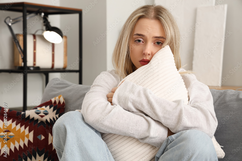 Depressed young woman with pillow sitting on sofa at home Depressed young woman with pillow sitting on sofa at home