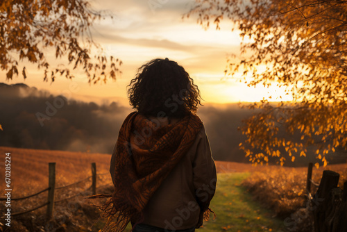 A young african american woman is walking happily with an autumn coat in a country landscape during sunset in autumn with no leaves on the trees