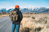 Tourist traveller with backpack standing into road in nature environment, back view of male hiker looking
