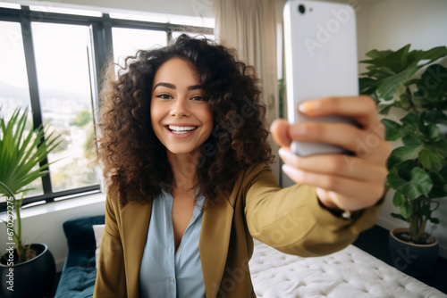 A young latin woman is is making a selfie while smiling with a telephone in a modern living room a high tech social media woman photo