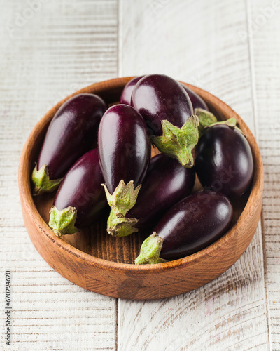 Fresh mini eggplant in a wooden plate on a white wooden background. Vegetables.