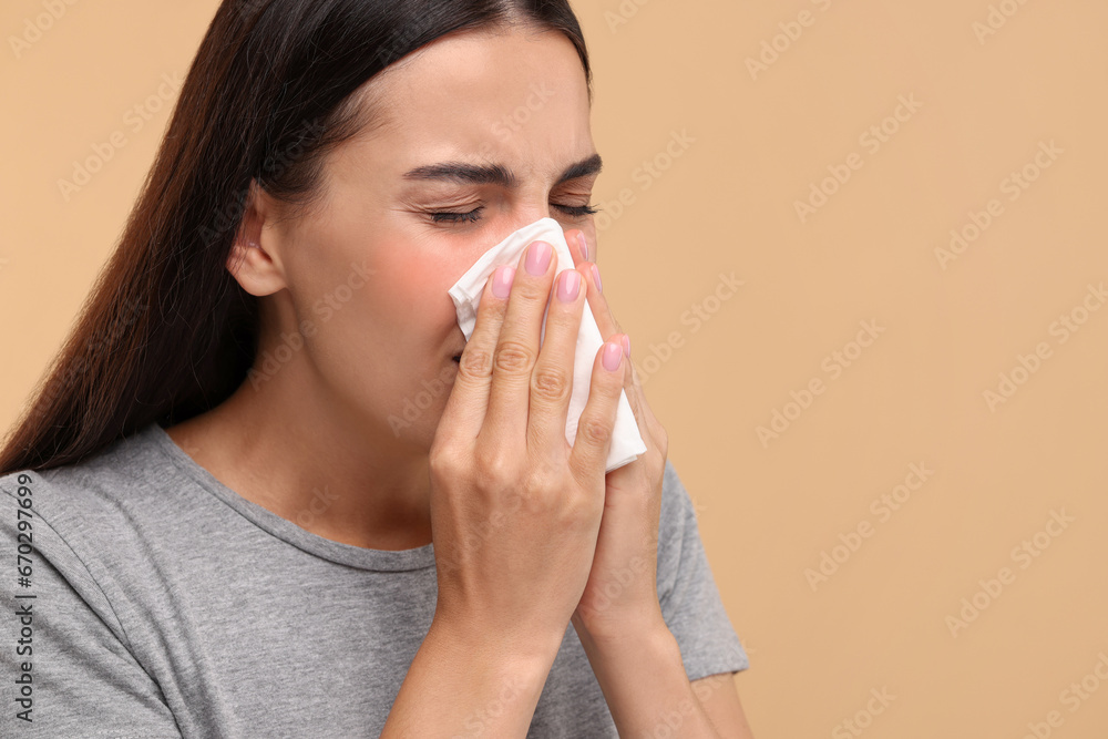 Suffering from allergy. Young woman blowing her nose in tissue on beige background, closeup. Space for text Suffering from allergy. Young woman blowing her nose in tissue on beige background, closeup. Space for text