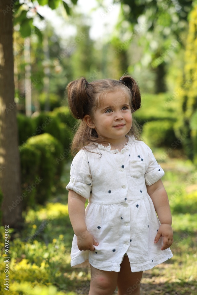Cute little girl walking near green plants in park Cute little girl walking near green plants in park