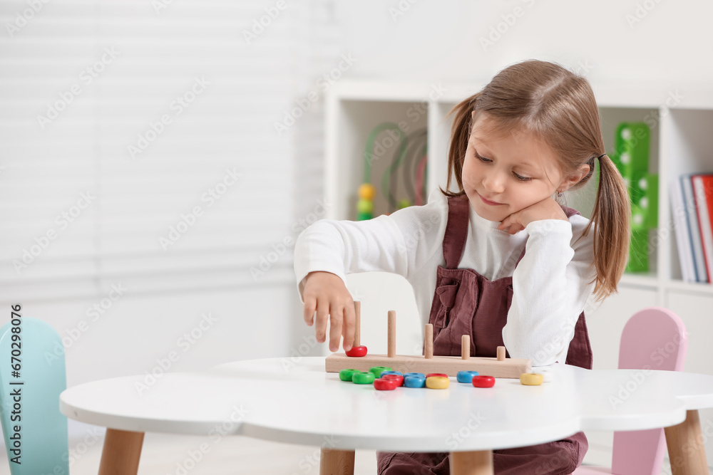 Cute little girl playing with stacking and counting game at white table indoors, space for text. Child's toy Cute little girl playing with stacking and counting game at white table indoors, space for text. Child's toy