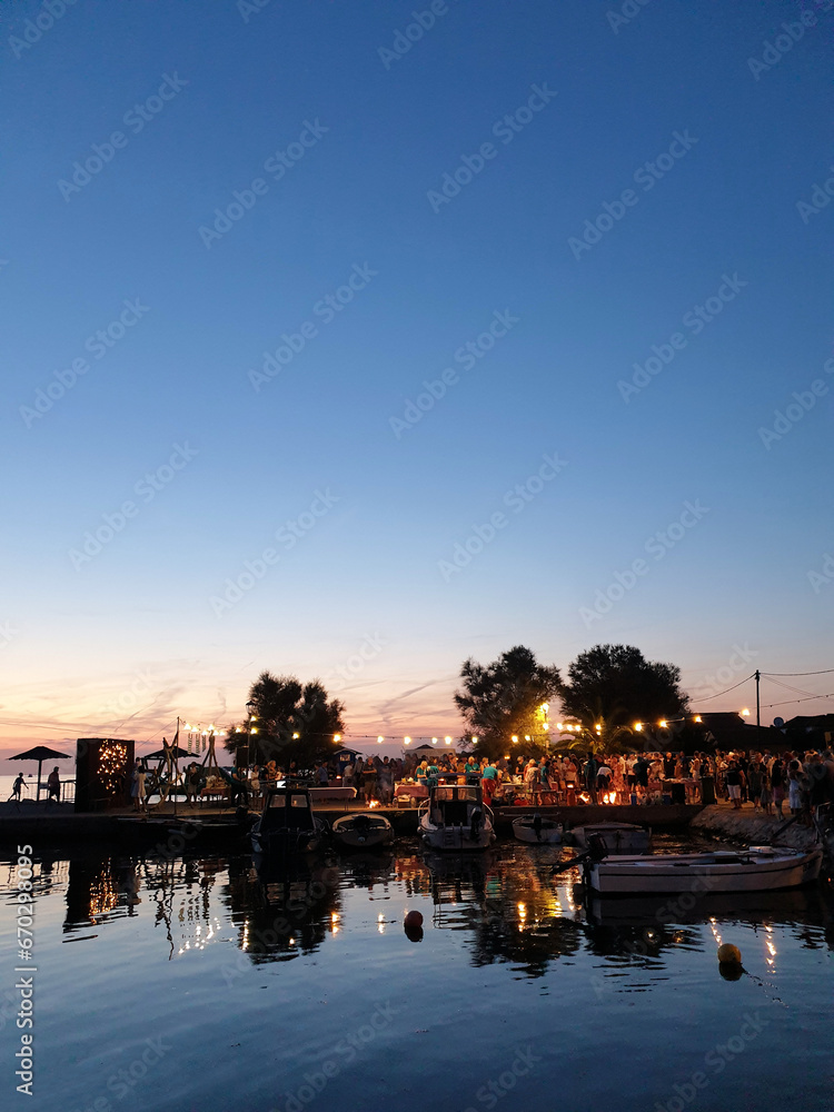 silhouette of people standing on pier next to harbor having fun enjoying festival against sunset sky in Croatia