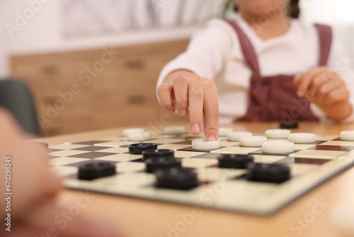 Girl playing checkers at table in room  closeup