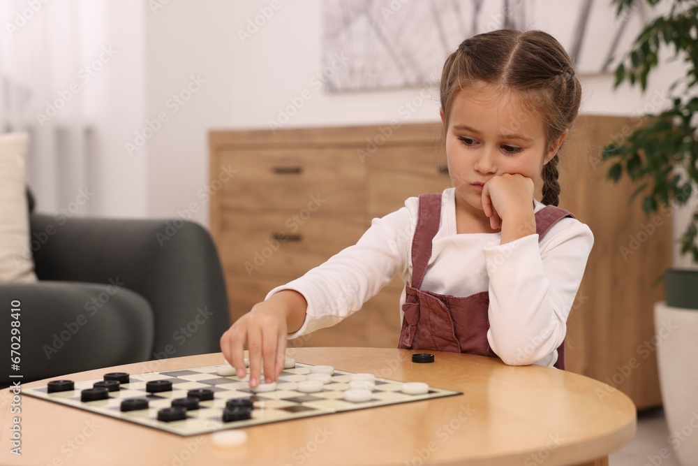 Thoughtful girl playing checkers at wooden table in room