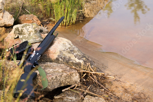 Hunting rifle and cartridges on rocks near lake outdoors. Space for text