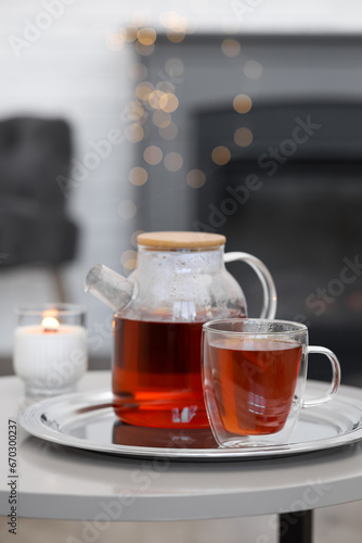Teapot, cup of aromatic tea and burning candle on white table indoors, space for text