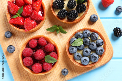Tartlets with different fresh berries on light blue wooden table, flat lay. Delicious dessert