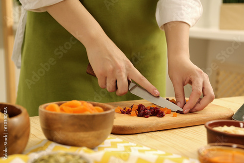 Making granola. Woman cutting dried apricots and cherries at table in kitchen, closeup