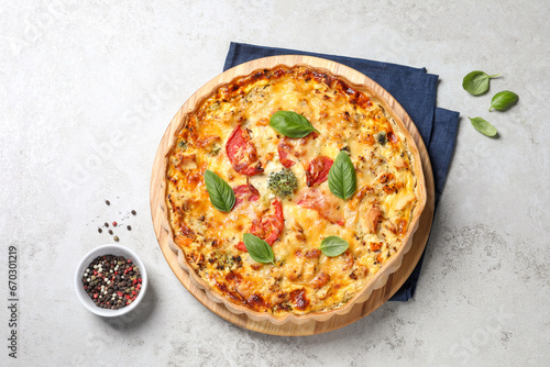 Tasty quiche with cheese, tomatoes and basil leaves on light grey table, flat lay