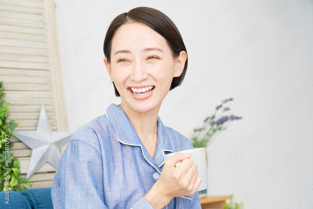 リビングでパジャマ姿で温かい飲み物を飲む女性
