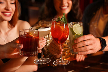 Friends clinking glasses with fresh cocktails in bar, closeup