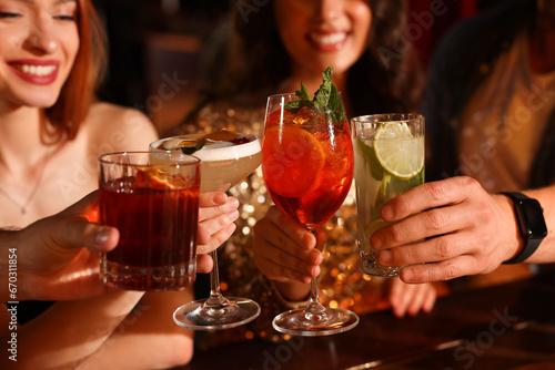 Friends clinking glasses with fresh cocktails in bar, closeup