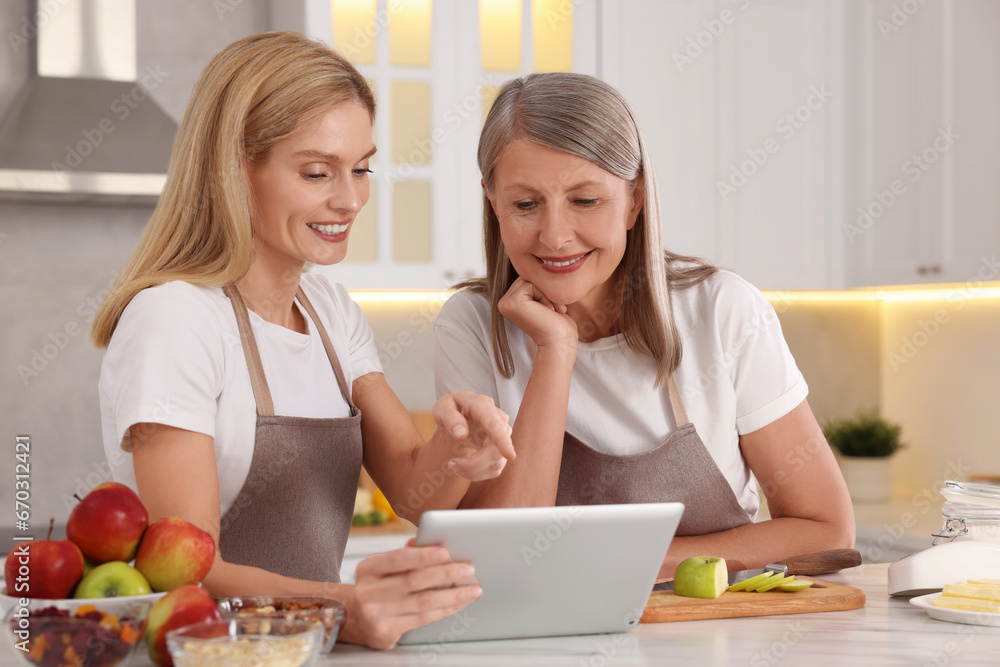 Happy mature mother and her daughter using tablet while cooking in kitchen Happy mature mother and her daughter using tablet while cooking in kitchen
