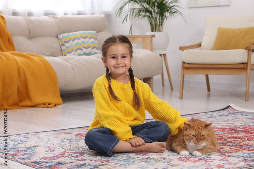 Smiling little girl petting cute ginger cat on carpet at home Smiling little girl petting cute ginger cat on carpet at home