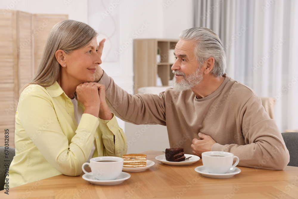 Affectionate senior couple having breakfast at wooden table in room Affectionate senior couple having breakfast at wooden table in room