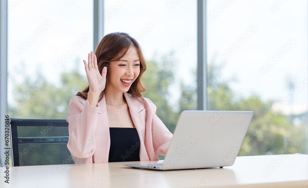 Asian professional successful young female businesswoman secretary in casual business suit sitting at workstation desk typing working with laptop notebook computer in company office at glass windows Asian professional successful young female businesswoman secretary in casual business suit sitting at workstation desk typing working with laptop notebook computer in company office at glass windows