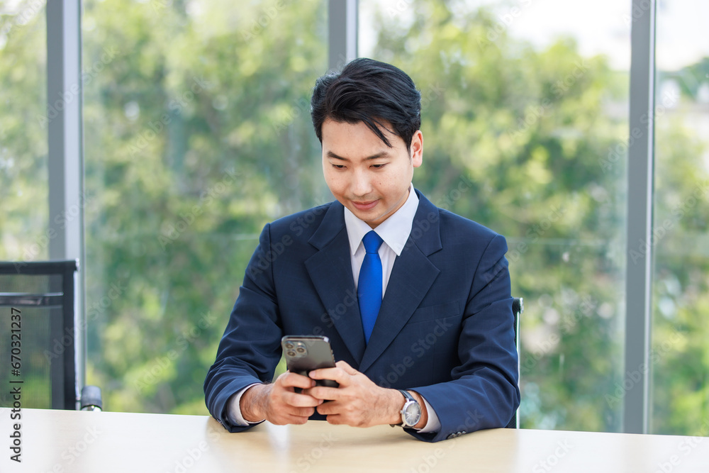 Asian professional successful male businessman employee in formal business suit sitting working using mobile phone in company office meeting room with graphs charts on big computer monitor screen Asian professional successful male businessman employee in formal business suit sitting working using mobile phone in company office meeting room with graphs charts on big computer monitor screen