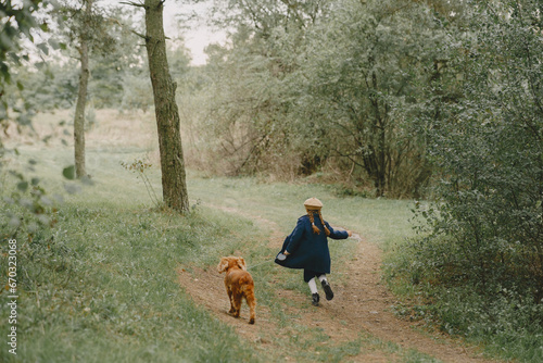 Little girl walks in autumn forest with a dog