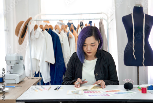 young cool female designer with purple color hair concentrate to create sketching and color comparison of clothing design on table,a professional dressmaker working in modern fashion studio