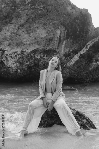Fototapeta Naklejka Na Ścianę i Meble -  Beautiful girl in a classic suit posing on the ocean shore while standing in the waves