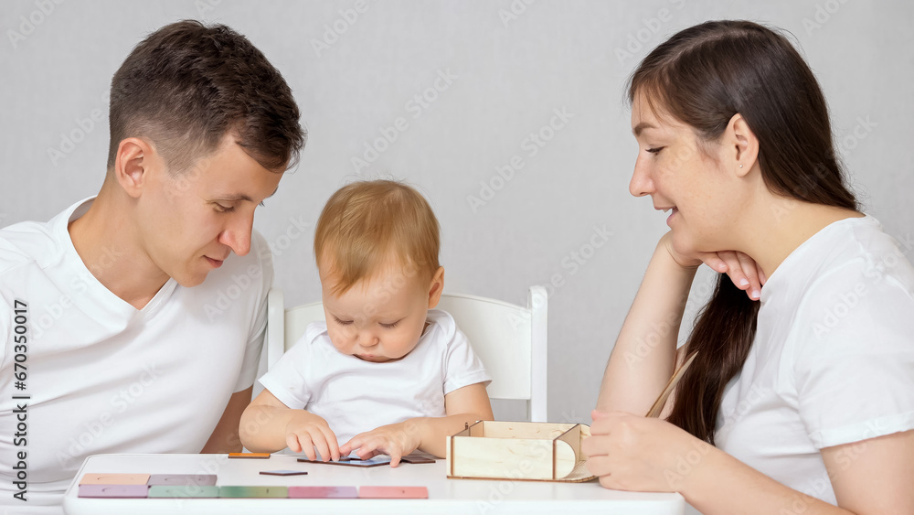 Parents help toddler daughter in educational game with cards in light room. Family members play together with child to develop thinking concept Parents help toddler daughter in educational game with cards in light room. Family members play together with child to develop thinking concept