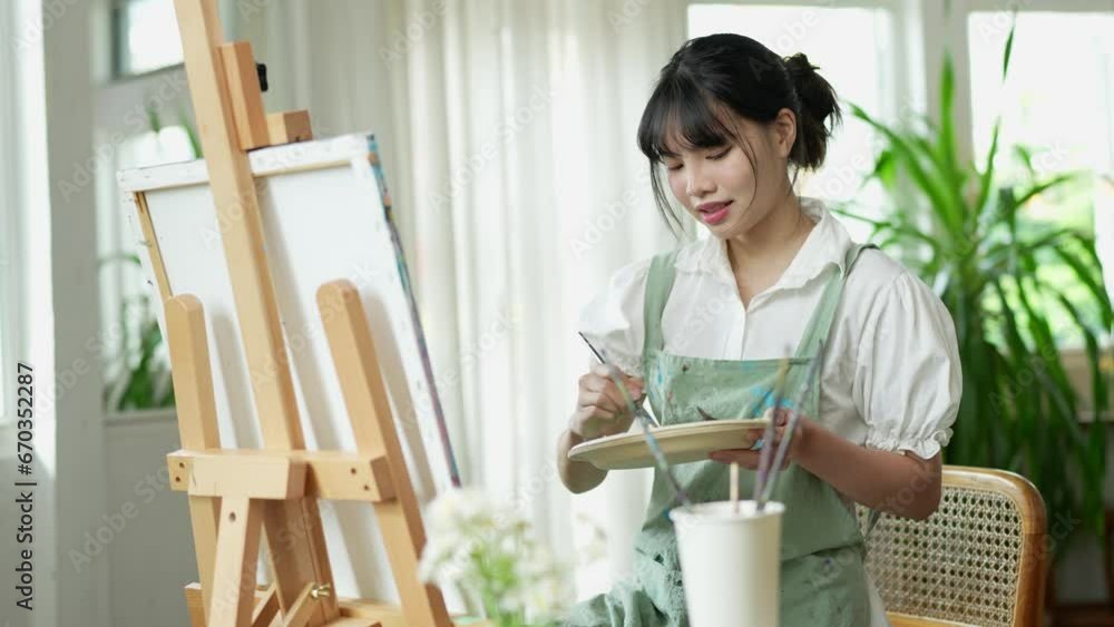 Young Asian female artist holds a palette with mixed acrylic paints. Use your creativity in designing pictures. Create art on canvas Develop art drawing skills Hobby activities in the studio or home. Young Asian female artist holds a palette with mixed acrylic paints. Use your creativity in designing pictures. Create art on canvas Develop art drawing skills Hobby activities in the studio or home.