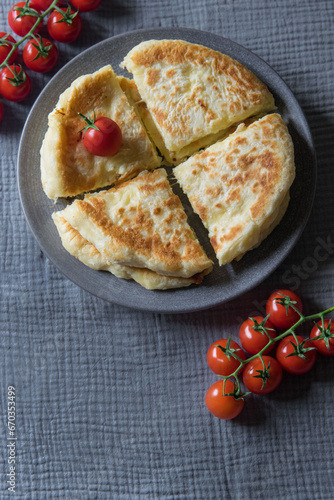 Homemade cheese filled savoury pies khachapury on grey plate served with tomatoes. Selective focus
