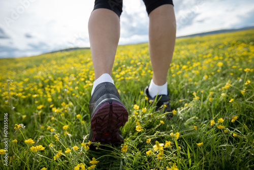 Woman runner legs on flowers trail on high altitude grassland