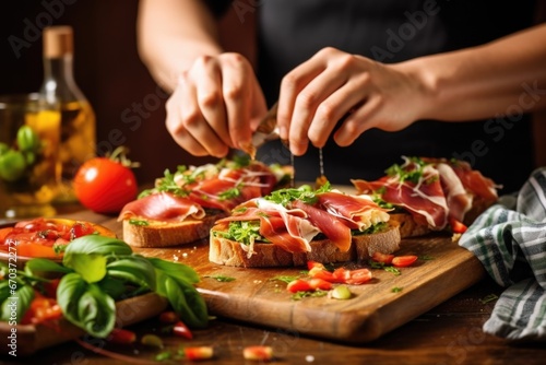 hands layering fresh bruschetta with prosciutto