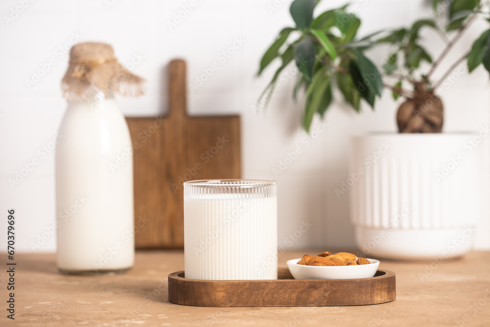 Organic almond milk in glass near the bowl with raw almonds on the table in the kitchen ready for cooking Organic almond milk in glass near the bowl with raw almonds on the table in the kitchen ready for cooking